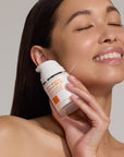 Person holding Daily Defense Mineral SPF 50 Facial Sunscreen to the side of their cheek.