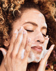 Woman washing her face with lots of soap suds.