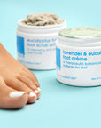 A model foot with Lavender and Eucalyptus Foot Creme and Eucalyptus Foaming Foot Scrub in background