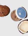 Open jar of Coconut Foaming Body Scrub next to a pieces of a cracked open raw coconut