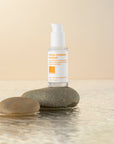 Clear bottle of hyaluronic acid sat on a rock surrounded by shallow water.
