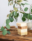 Stack of four LATHER soap bars next to a vase filled with eucalyptus branches
