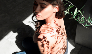 Woman facing away from a sunny window, the shadow of leaves on her shoulder