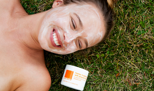 Model wearing Honey Moisture Mask laying in grass next to jar of Honey Moisture Mask