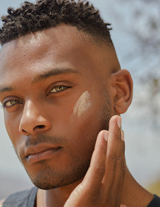 Male model applying sunscreen while gazing at the camera