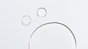Close up of droplets of clear serum product on light grey background. The lighting in the photo is strong, so the droplets cast the faintest shadow that causes black outlines around them. The result is organic-looking black circles. 