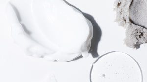 Close up of three different LATHER products, each with a different texture. One is white in color with a rich, creamy texture. One is a light purple-grey, with a grainy texture. One is clear with a glossy, smooth texture.