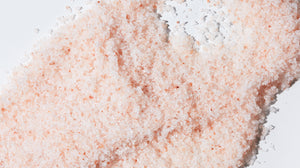 Close up of LATHER Muscle Ease Bath Salts, emphasizing peachy-pink color and crystalline texture.