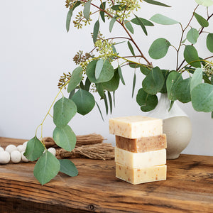 Stack of four LATHER soap bars next to a vase filled with eucalyptus branches